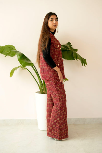Woman in a red patterned outfit standing next to a potted plant against a white wall.