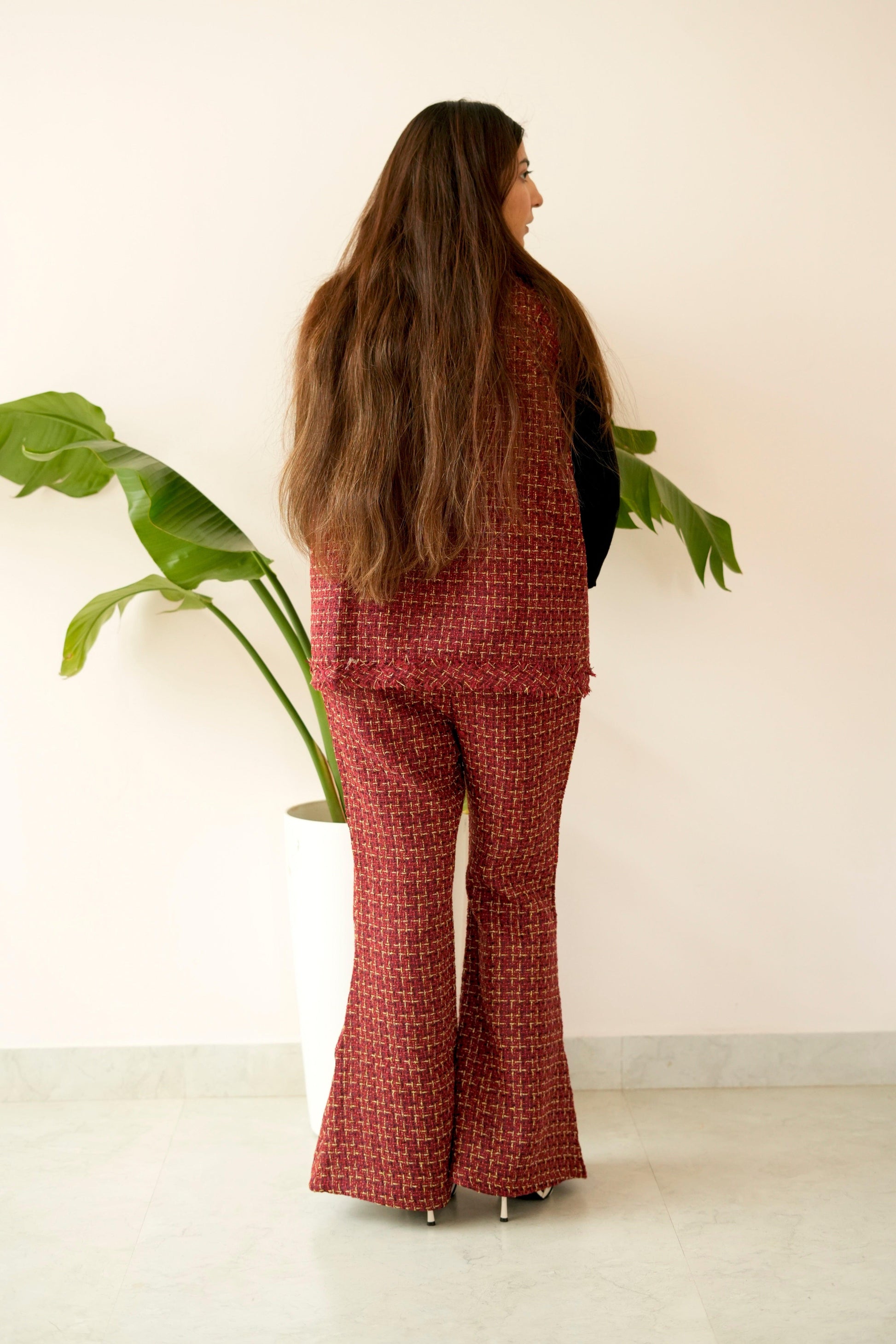 Person wearing a red patterned outfit standing in front of a white wall with a plant.