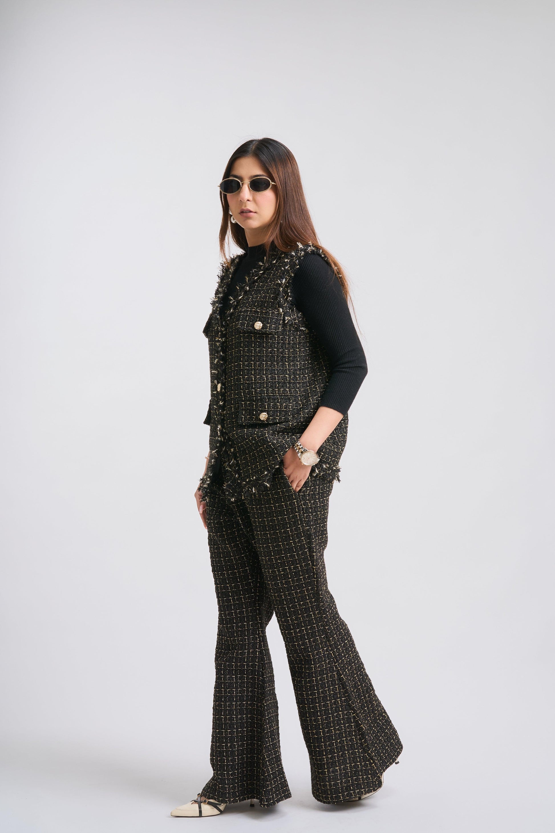 Woman wearing a black studded vest and flared pants on a white background