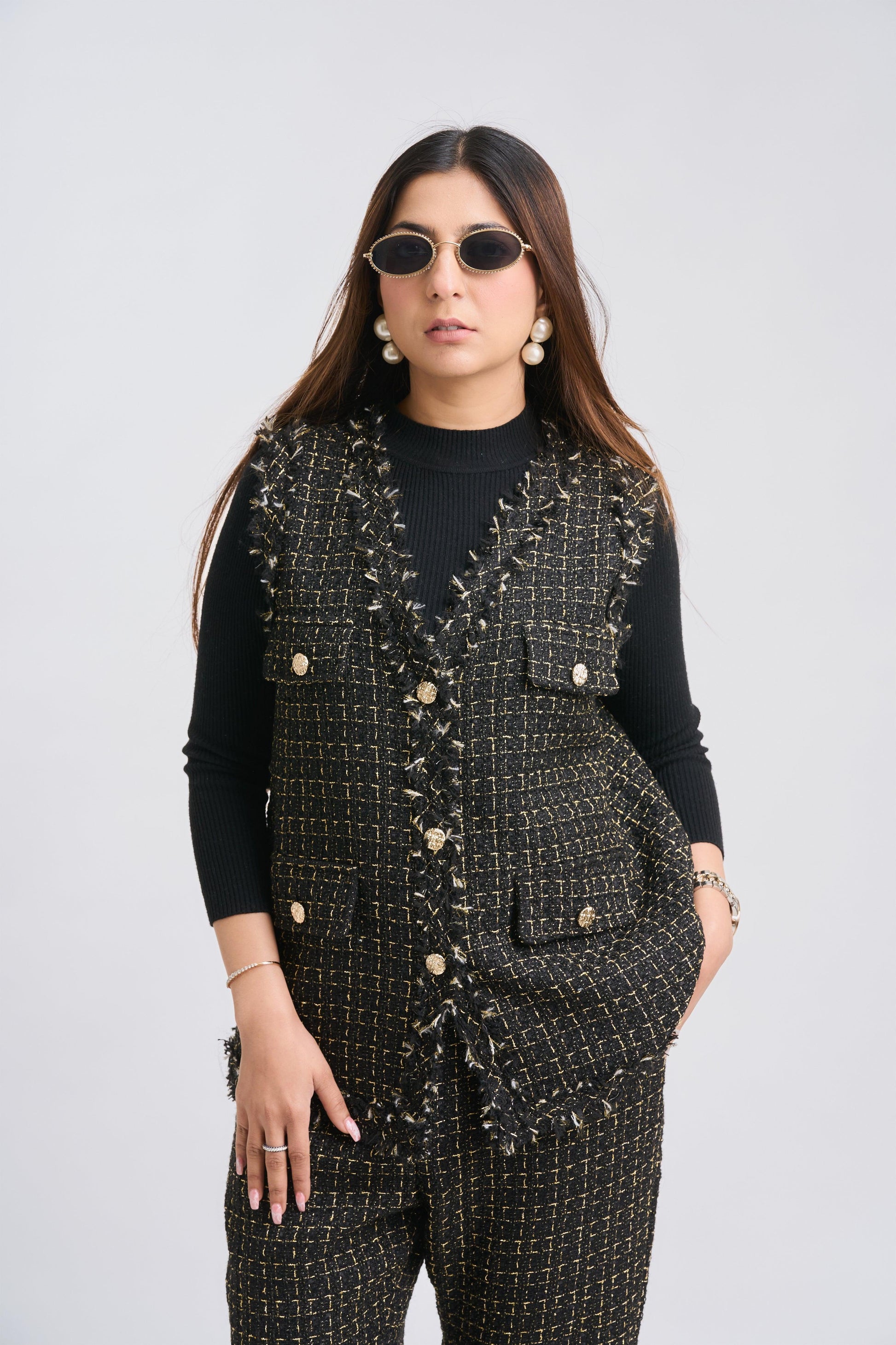 Woman wearing a black patterned vest over a black top on a white background