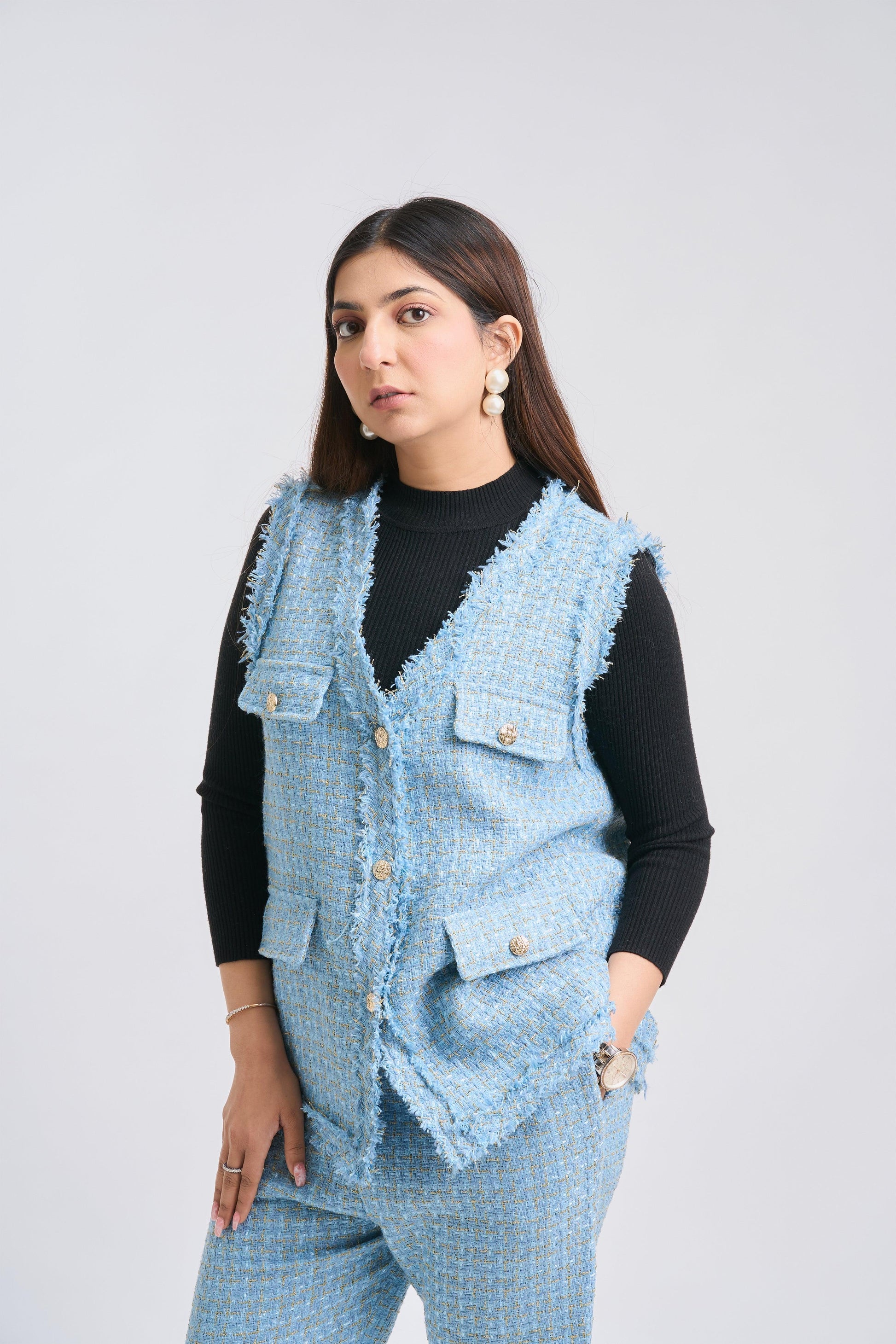 Woman wearing a light blue denim vest over a black top on a white background
