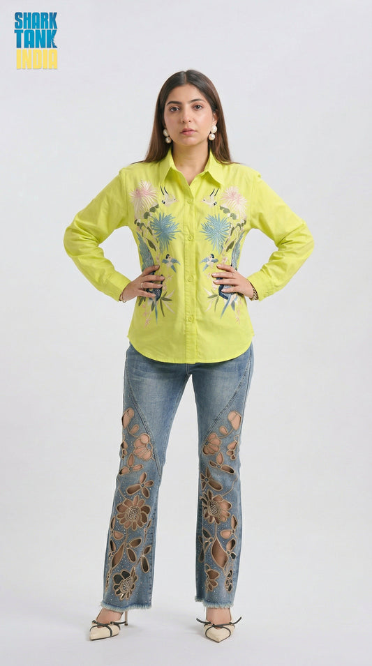 Woman wearing a bright yellow shirt with floral embroidery and blue jeans with floral patterns on a white background.