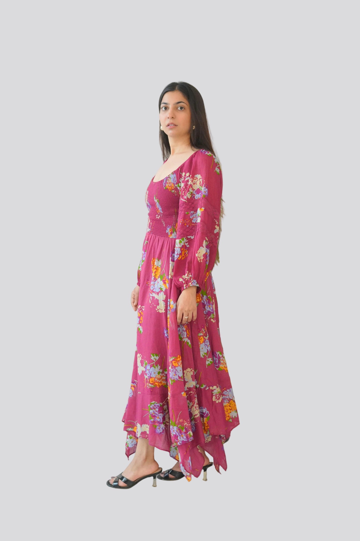 Person wearing a pink floral dress standing next to a large green plant indoors.