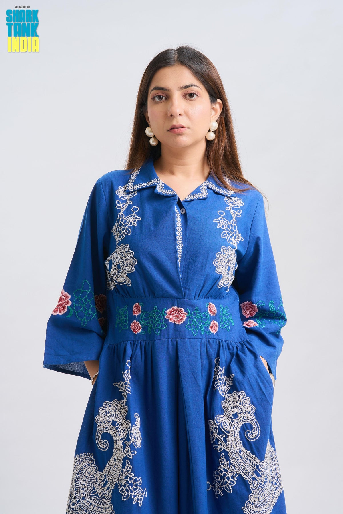 Woman wearing a blue embroidered dress against a white background