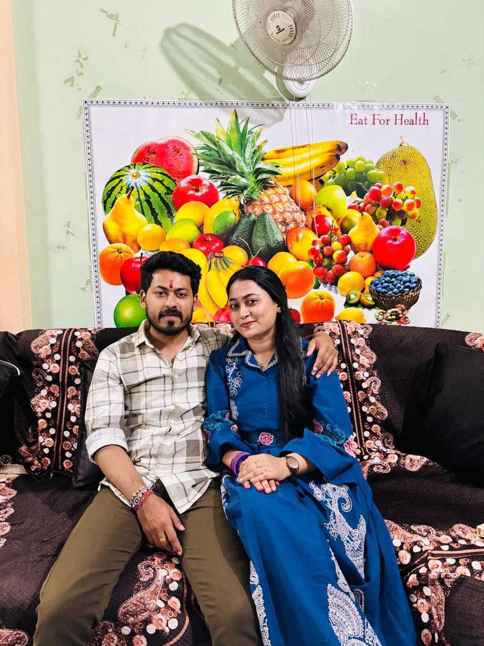 Two people sitting on a couch with a colorful fruit calendar in the background.