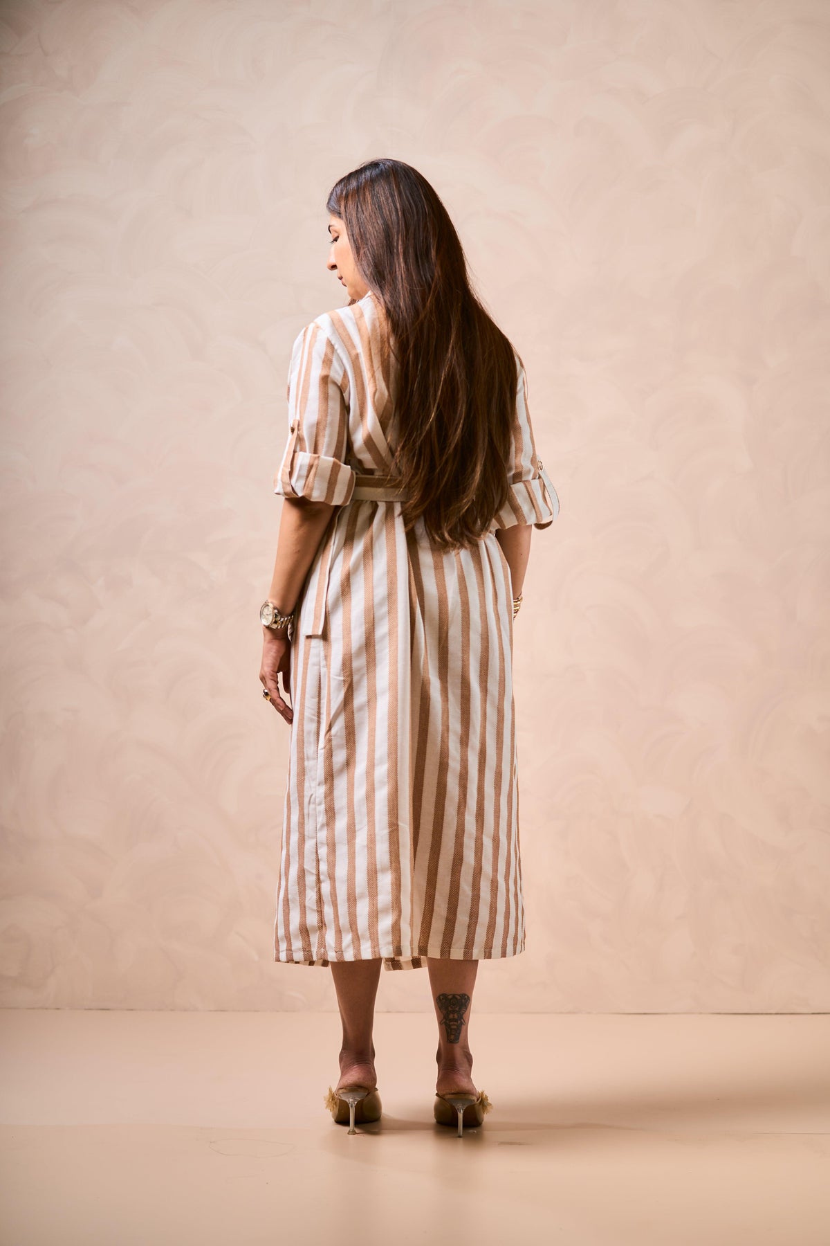 Woman wearing a striped dress standing against a beige background