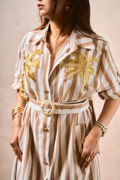 Woman wearing a striped dress with gold accents and jewelry against a beige background