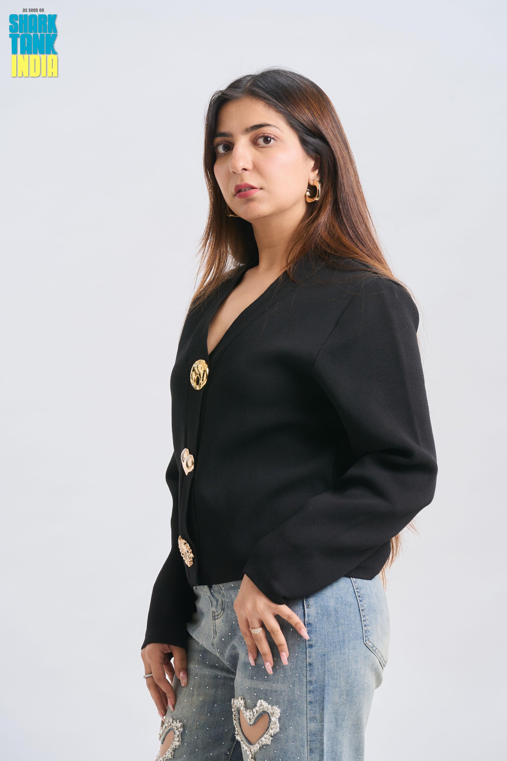 Woman wearing a black blazer with gold buttons on a light gray background