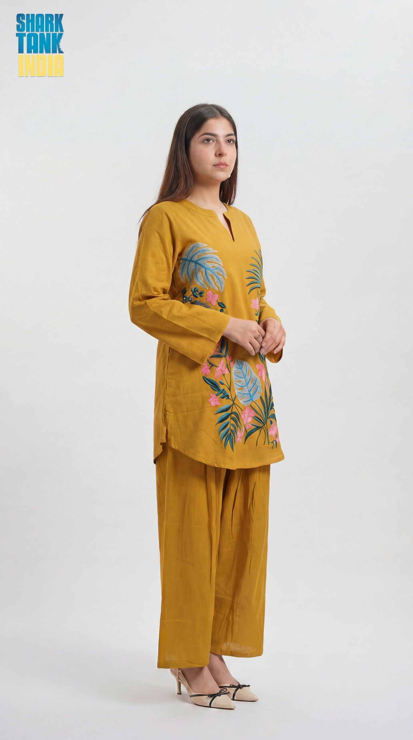 Woman wearing a mustard yellow outfit with floral embroidery on a white background