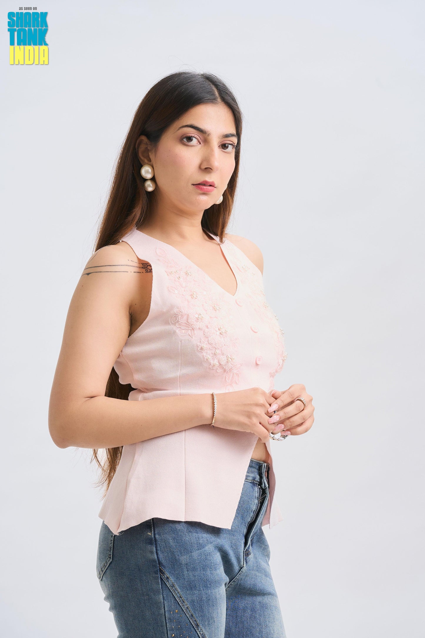 Woman wearing a light pink sleeveless top and blue jeans on a white background