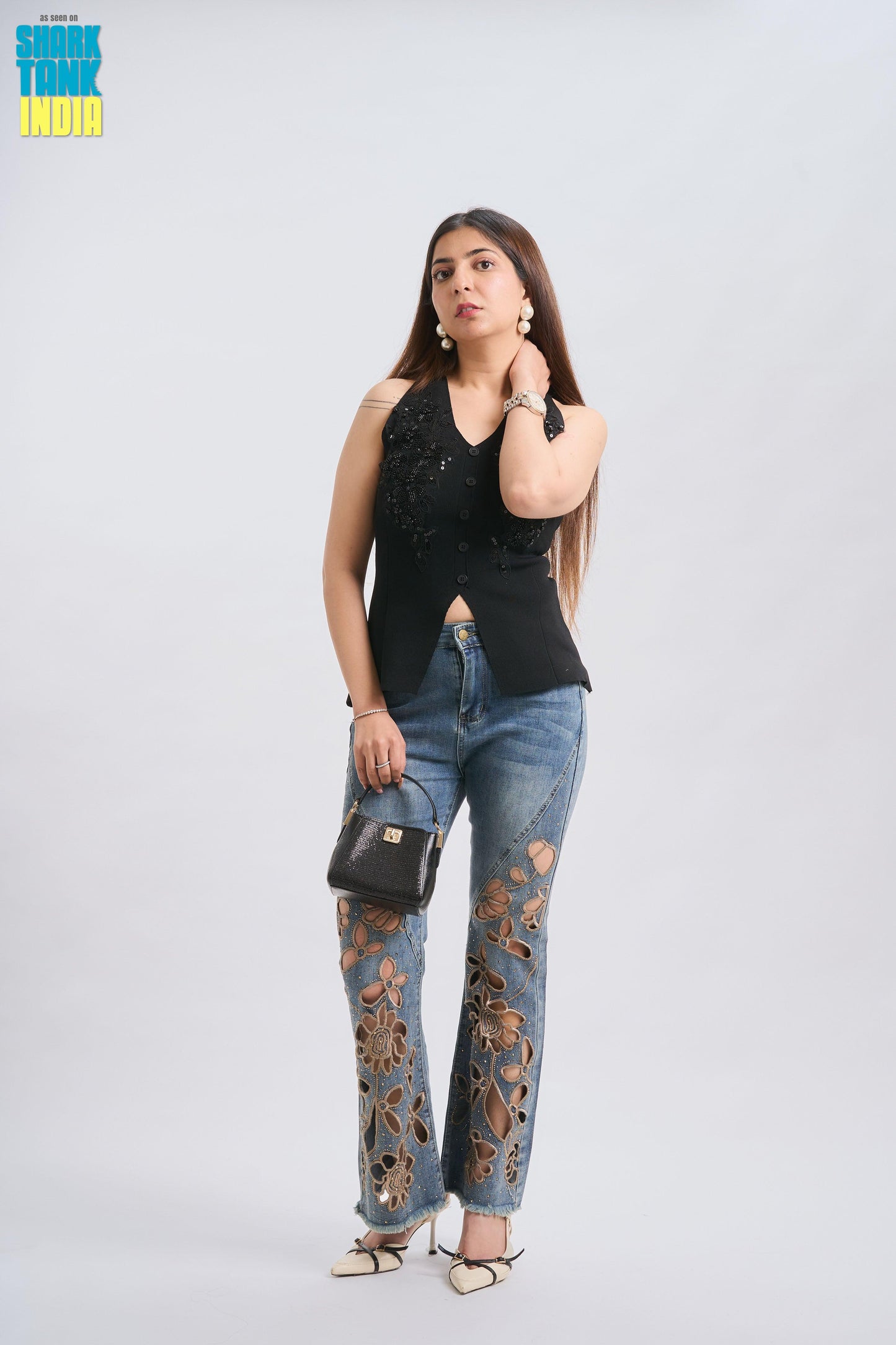Woman wearing a black sleeveless top and blue jeans with floral patterns on a white background