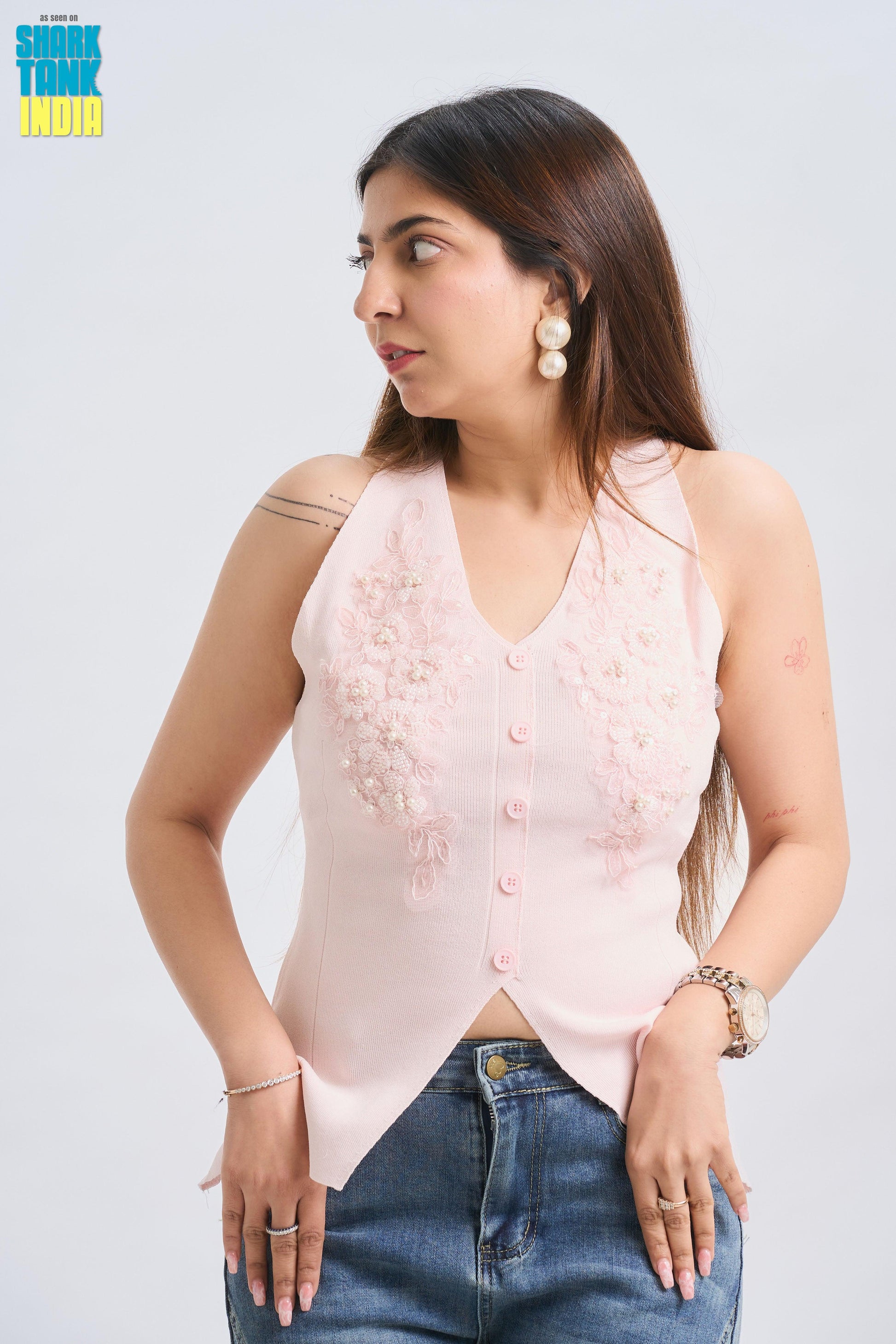 Woman wearing a light pink sleeveless top with buttons and blue jeans on a white background