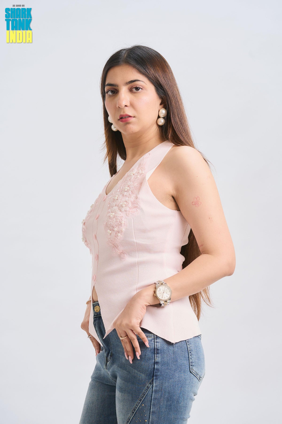 Woman wearing a light pink sleeveless top with lace details and blue jeans on a white background.