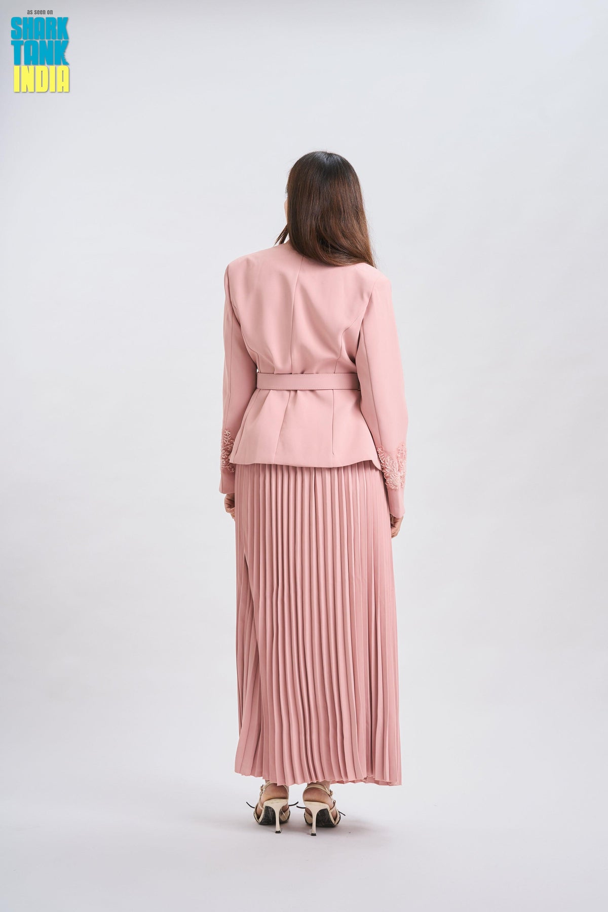 Woman wearing a pink outfit with a jacket and pleated skirt on a white background
