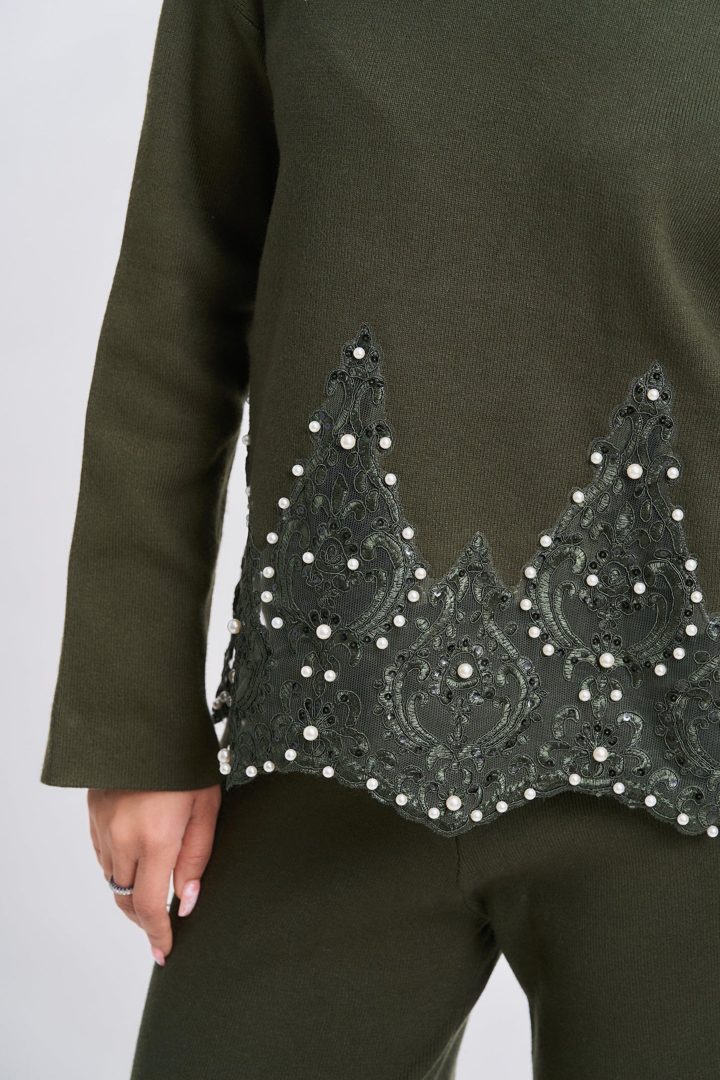 Green outfit with intricate black embroidery and pearl details on a plain background