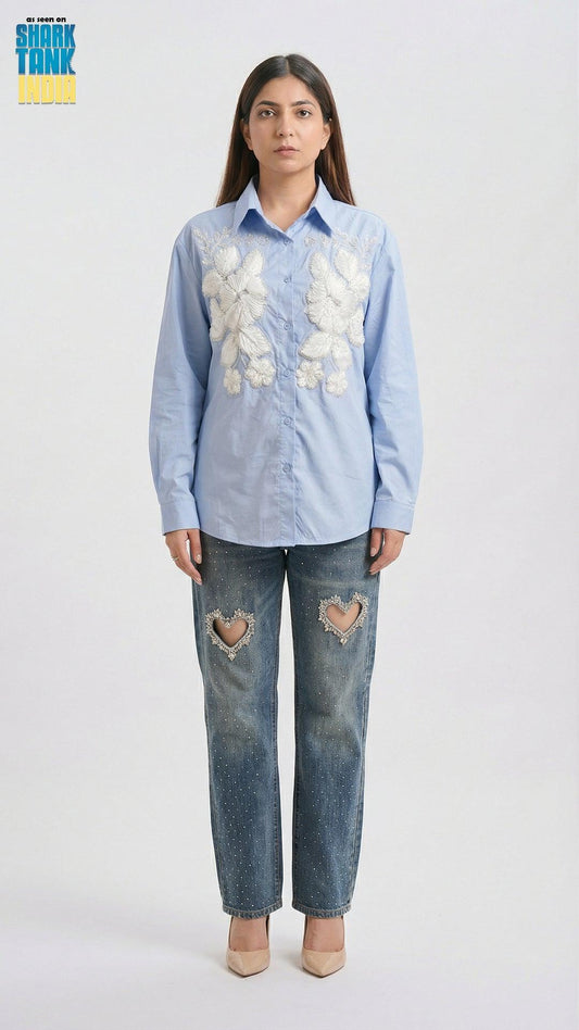 Woman wearing a light blue floral shirt and distressed jeans on a white background