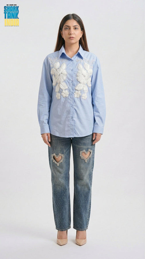 Woman wearing a light blue floral shirt and distressed jeans on a white background