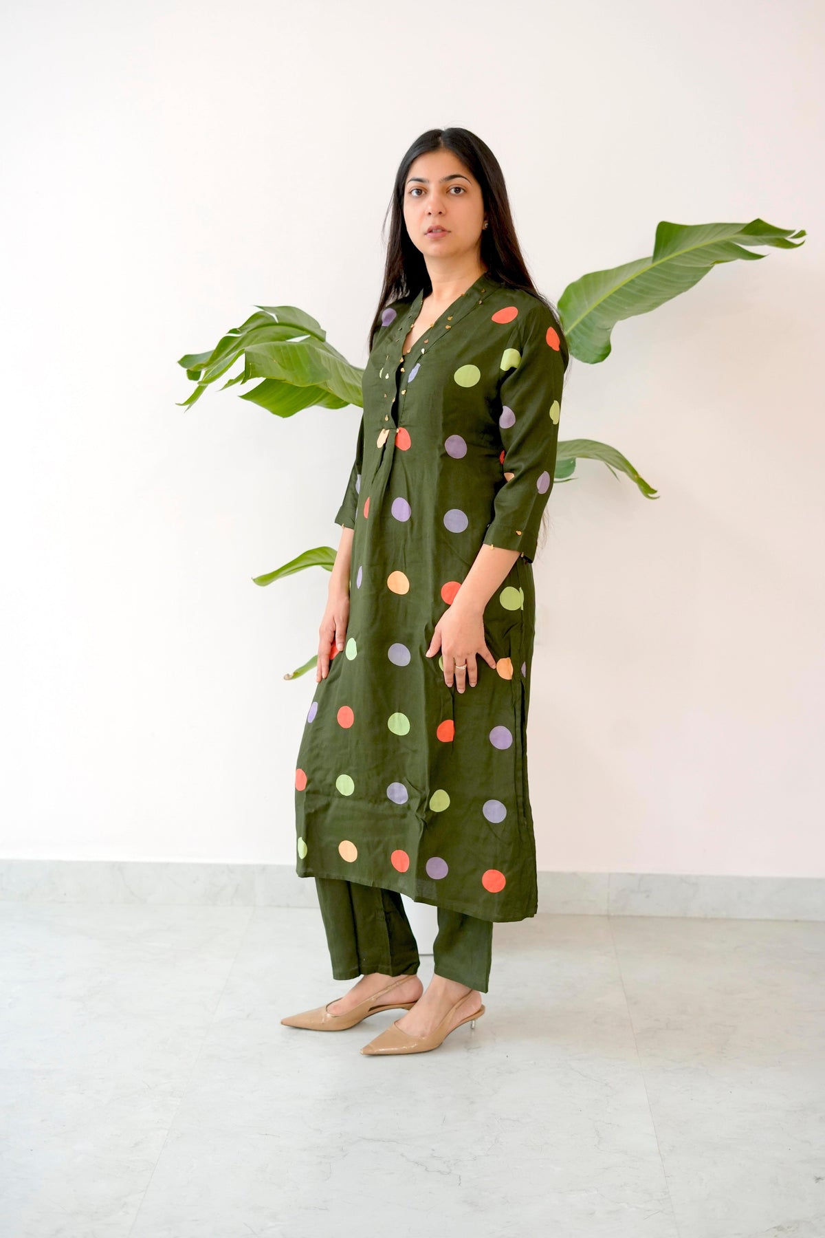 Woman wearing a green polka dot dress with a white background and plant decorations.