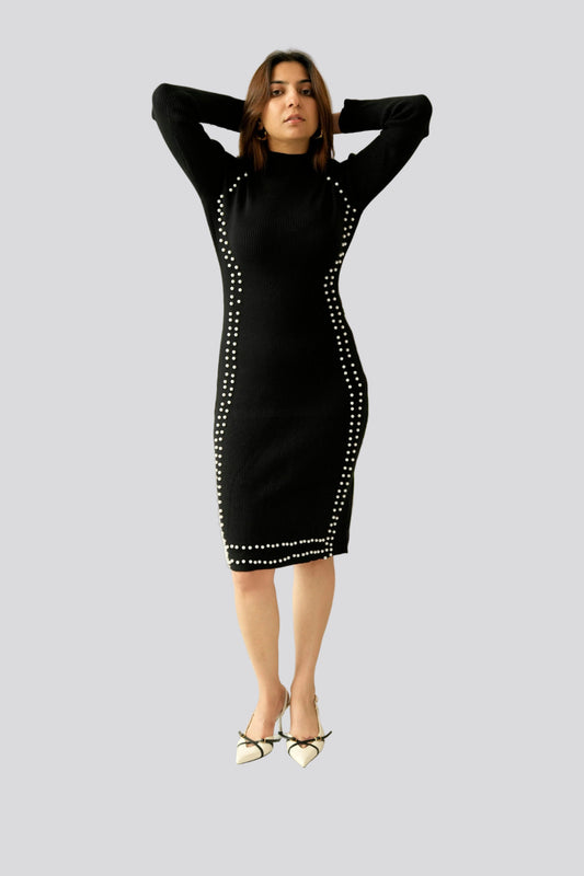 Woman wearing a black dress with white embellishments in a minimalistic setting.