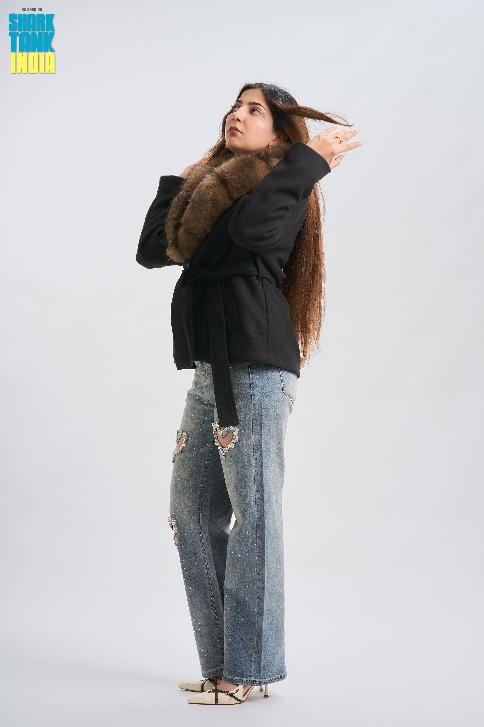 Woman wearing a black coat with fur trim and ripped jeans on a white background