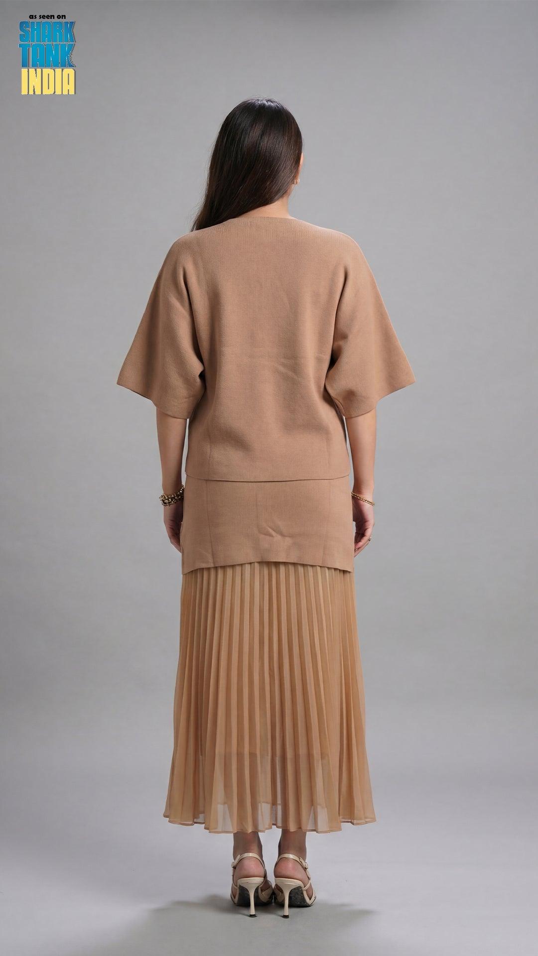 Woman wearing a beige outfit with a pleated skirt on a gray background