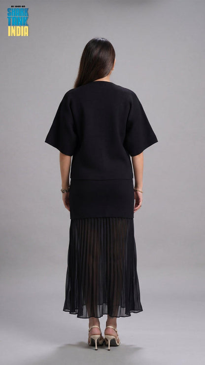 Person wearing a black outfit with a pleated skirt on a gray background