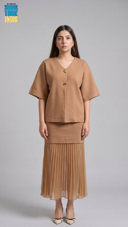 Woman wearing a brown outfit with a pleated skirt on a gray background
