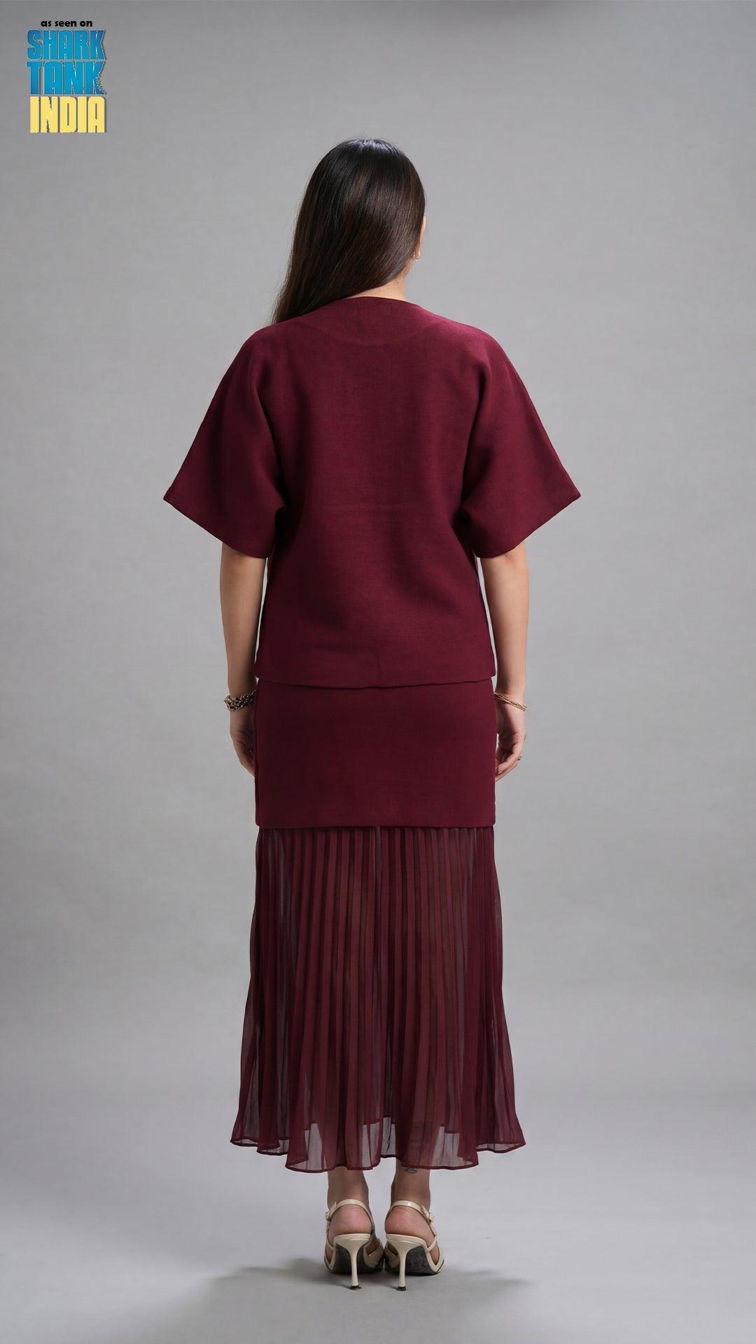 Person wearing a burgundy outfit with a pleated skirt on a gray background