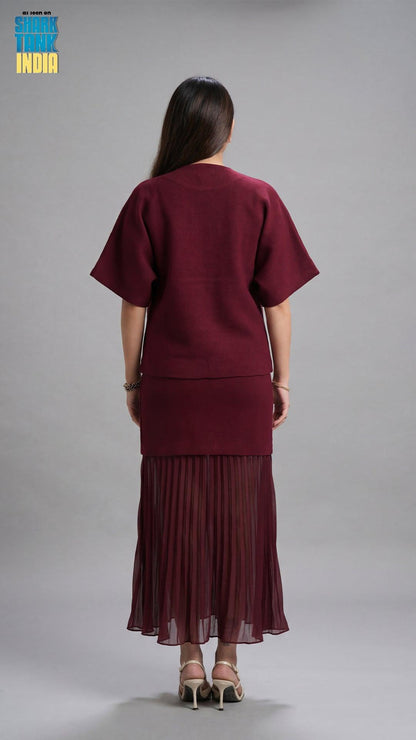 Person wearing a burgundy outfit with a pleated skirt on a gray background
