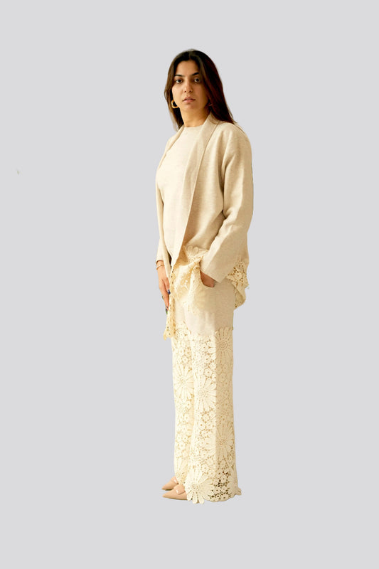Woman in a cream-colored outfit standing in a minimalistic room with a plant.
