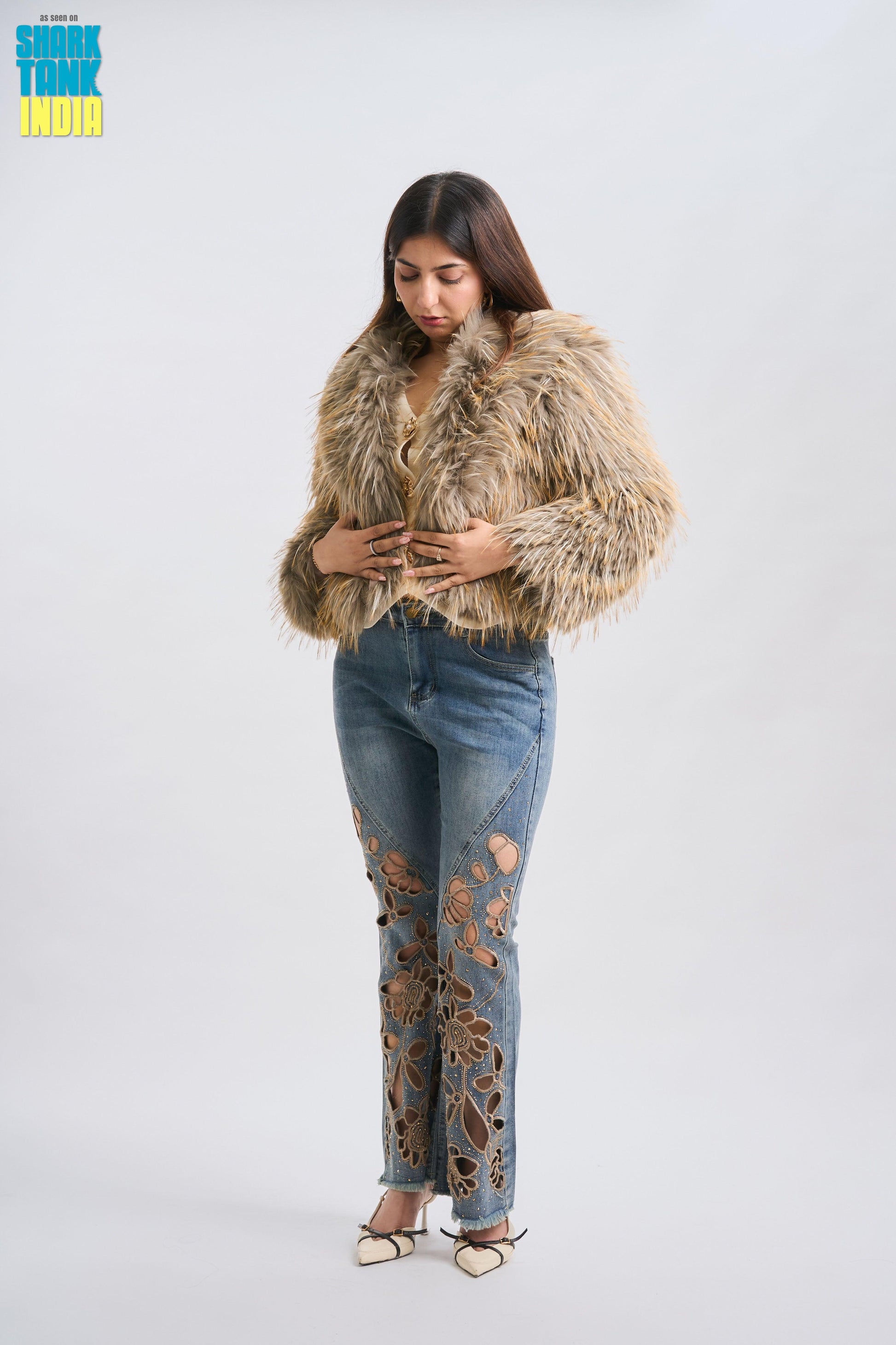 Woman wearing a fur coat and jeans with cut-out designs on a white background