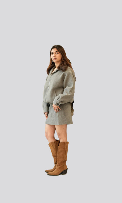 Woman wearing a gray coat and brown knee-high boots on a plain background