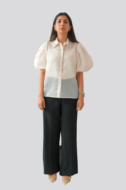 Woman wearing a white blouse and black pants standing in front of a plant