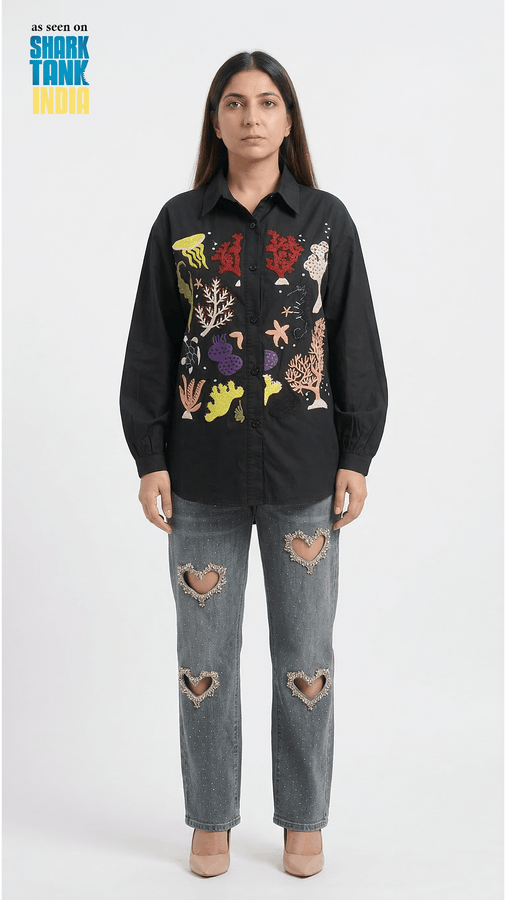 Person wearing a black shirt with colorful designs and ripped jeans on a white background