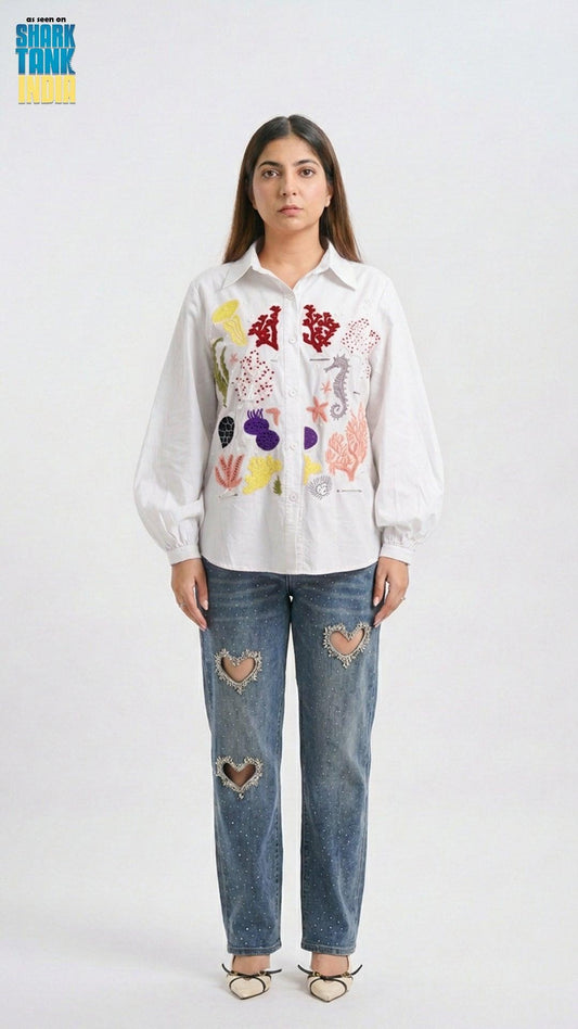 Woman wearing a white shirt with colorful floral patterns and blue jeans with heart patches on a white background.