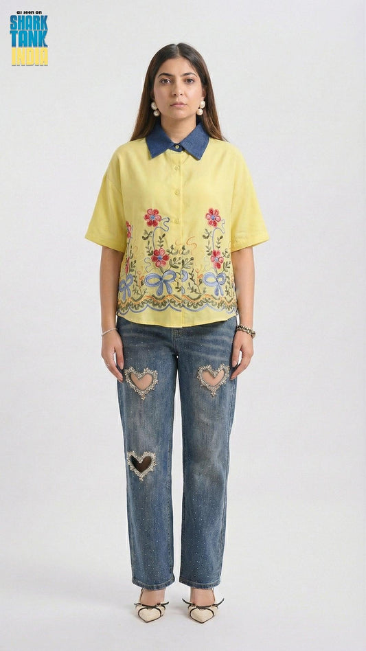 Woman wearing a yellow embroidered shirt and blue jeans on a white background