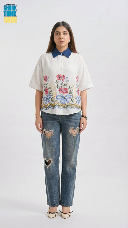Woman wearing a floral embroidered shirt and distressed jeans on a white background