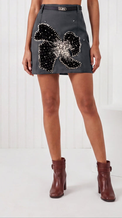 Woman wearing a white top and black skirt with a floral embellishment on a white background