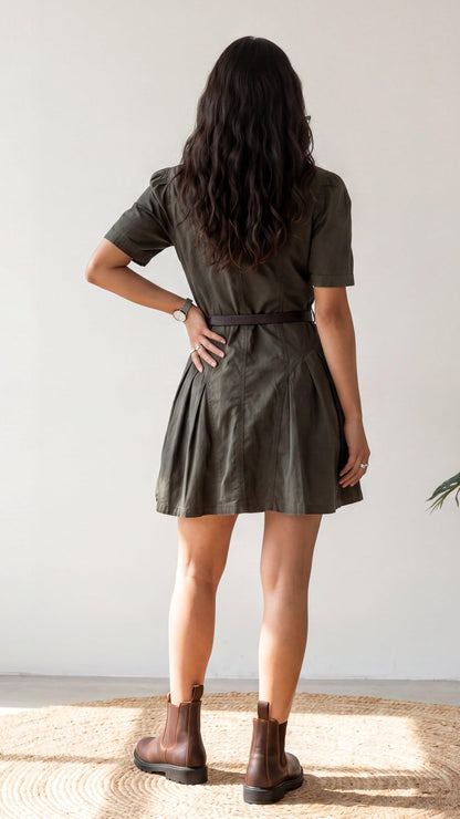 Person wearing a green dress standing with hands on hips against a plain background