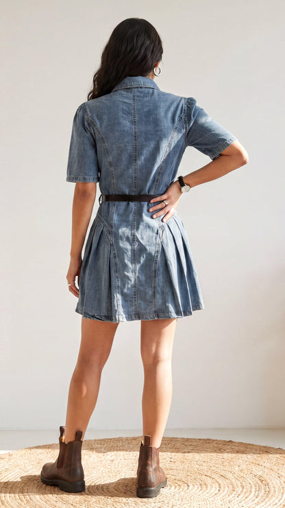 Person wearing a denim dress with a belt, standing on a woven mat against a plain background