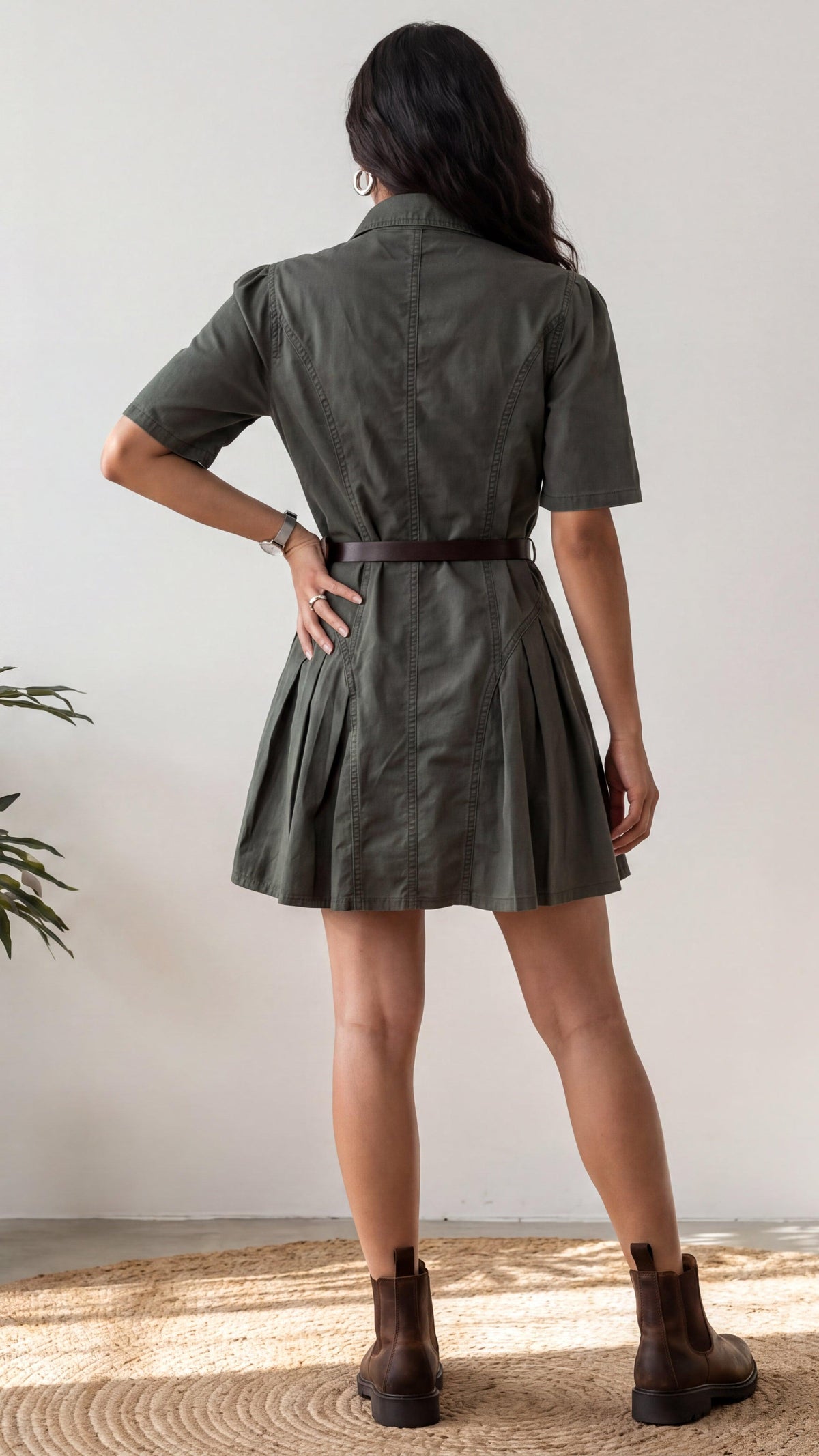 Woman wearing a green dress with a belt, standing against a plain background