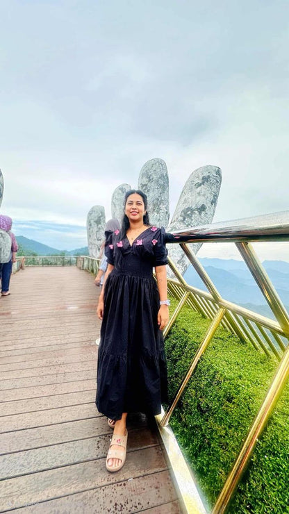 Woman in a black dress standing on a wooden platform with a scenic background