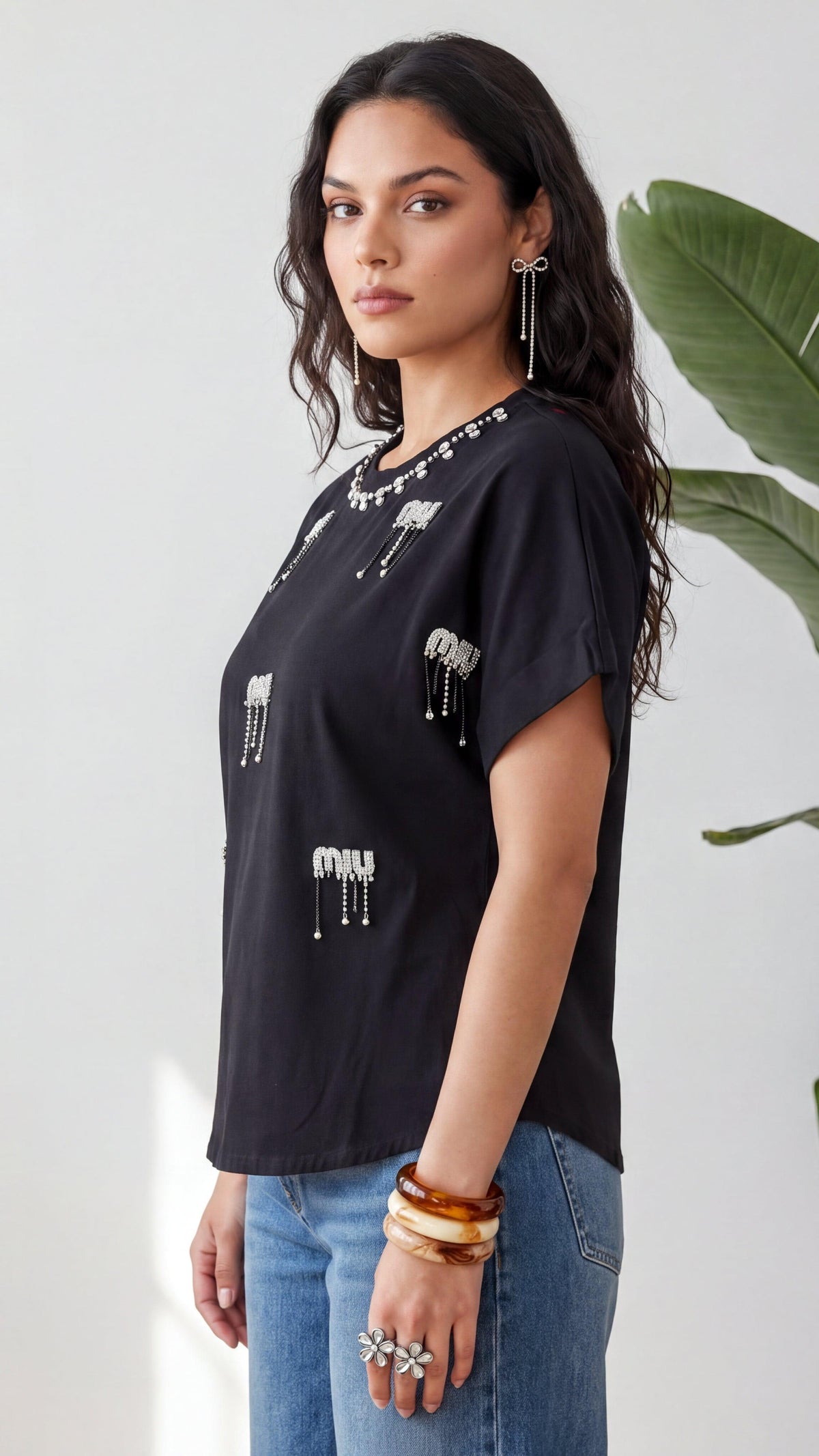 Woman wearing a black t-shirt with white patterns and blue jeans, standing against a light background.