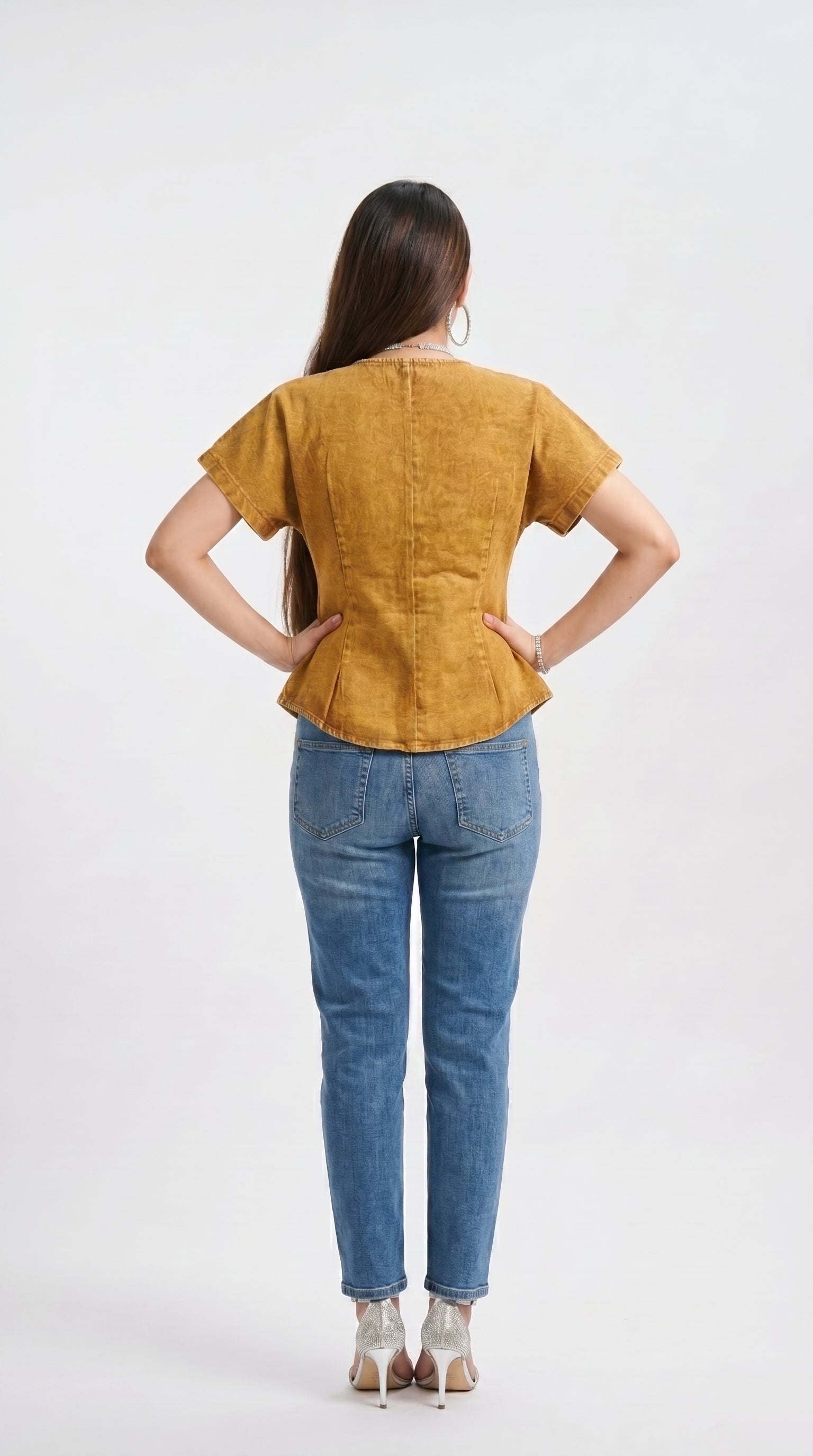 Woman wearing a mustard yellow top and blue jeans on a white background