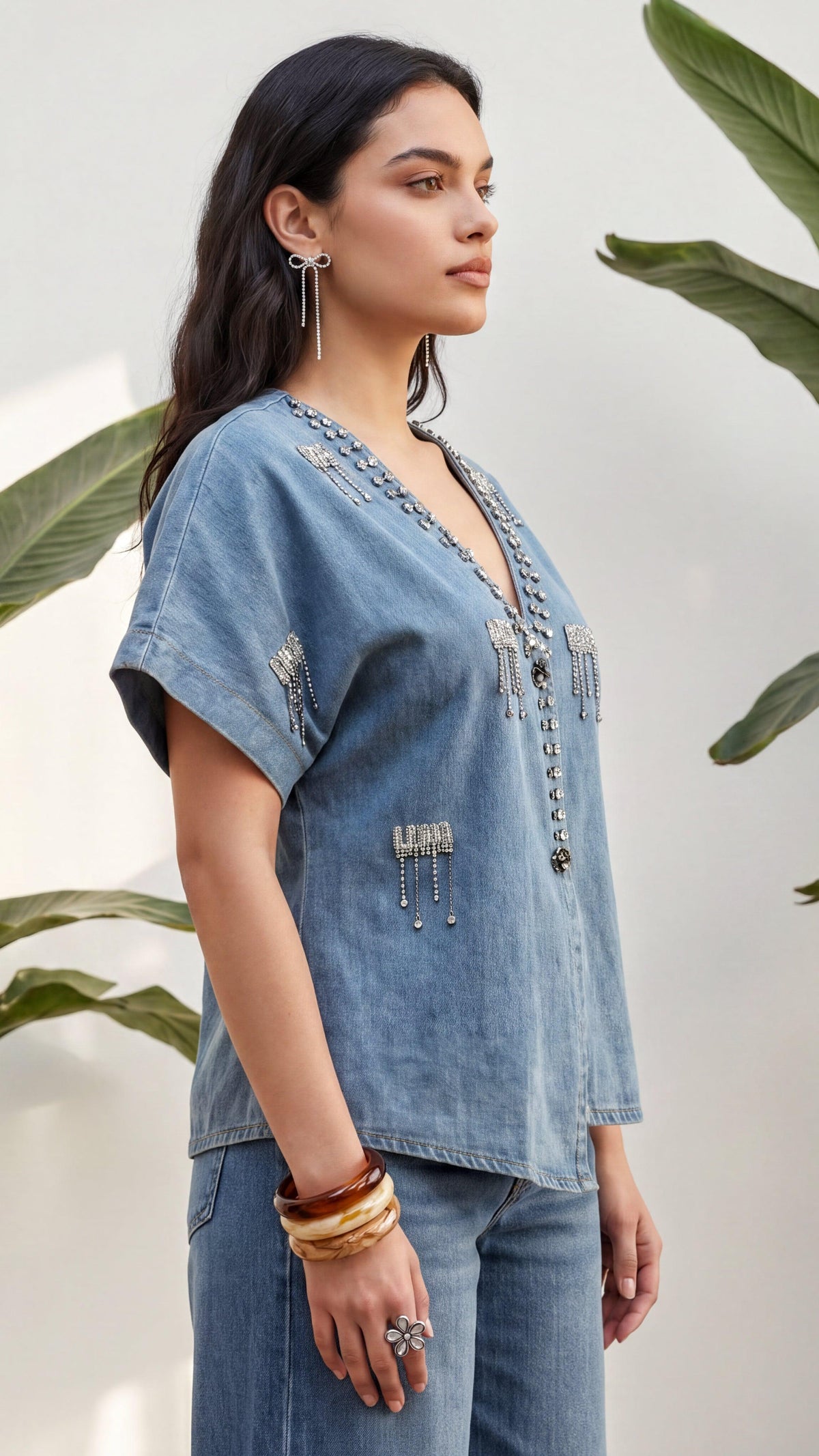 Woman wearing a denim top with embellishments against a neutral background