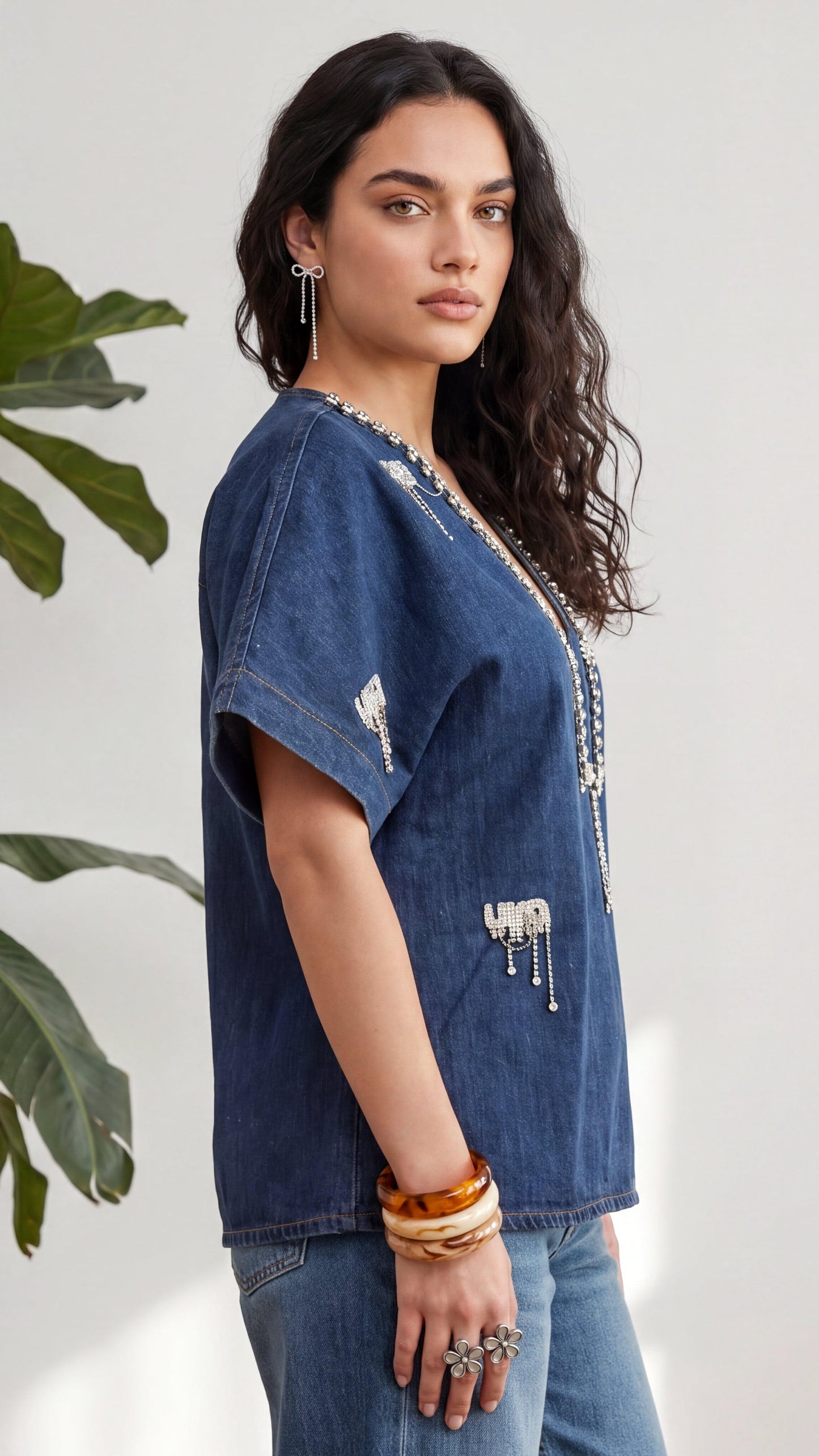 Woman wearing a blue denim shirt with decorative elements, standing against a light background.