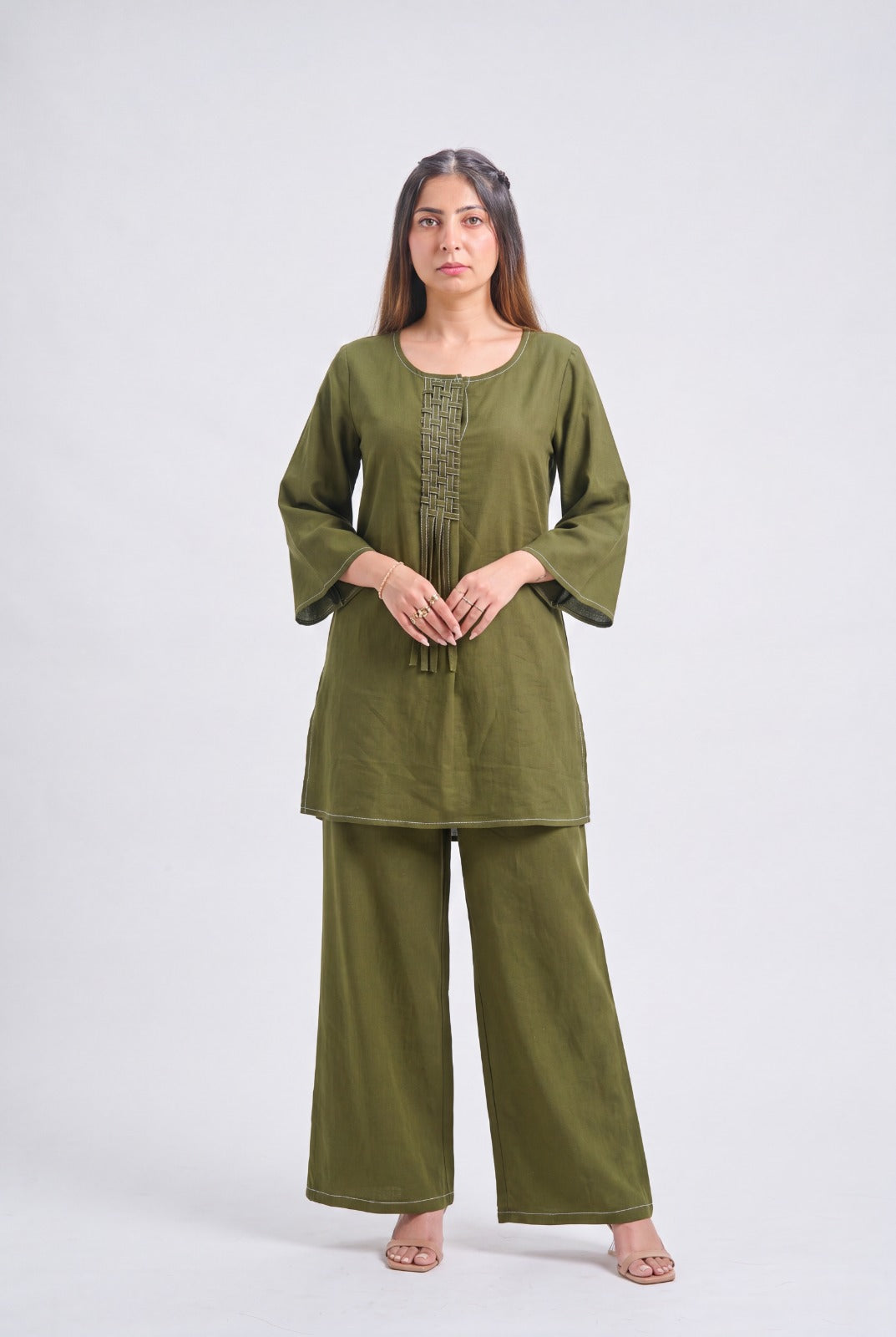 A woman modeling an olive green two-piece kurta set with wide-leg pants and three-quarter sleeves, standing against a light gray studio background.
