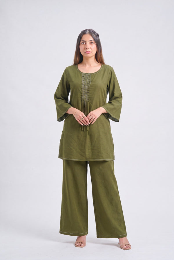A woman modeling an olive green two-piece kurta set with wide-leg pants and three-quarter sleeves, standing against a light gray studio background.