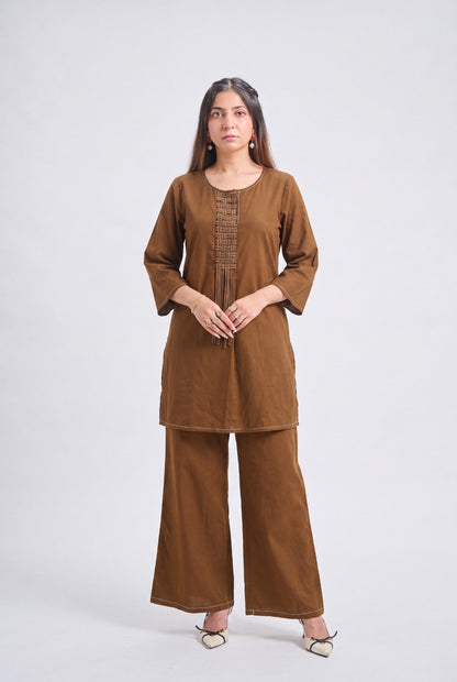 A woman modeling a brown two-piece kurta and trouser set against a plain light gray studio background.