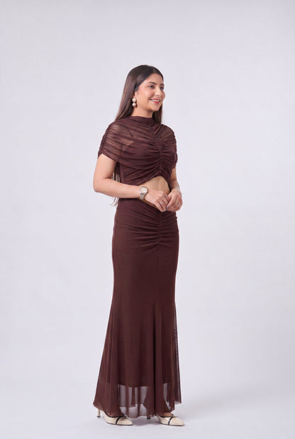 A woman modeling a dark brown two-piece set consisting of a short-sleeve cropped top and a matching floor-length skirt, photographed against a light gray studio background.